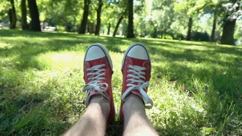 View of male's feet in red trainers lying on the grass, slow motion shot at 240f Stock Footage