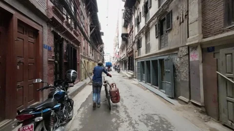 View of a man pushing a bicycle in a narrow street, Nepal. Video stock 335475893