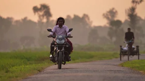 View of a man riding a motorcycle on a rural road, Bangladesh. 스톡 동영상 334968874