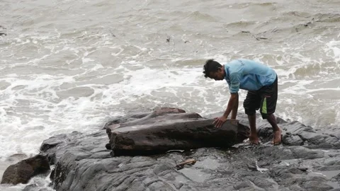 View of man trying to push large rock into sea water Video stock 191446645