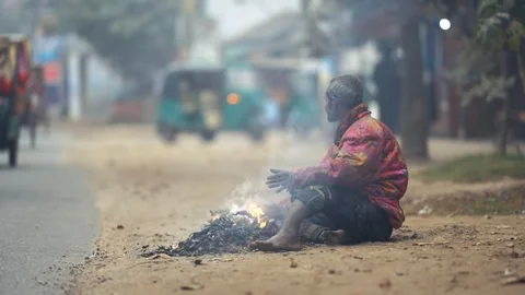 View of a man warming himself by a fire on a misty road, Bangladesh. Video stock 335550991