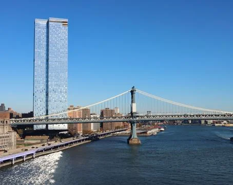 View of the Manhattan bridge next to a skyscraper on a sunny day Stock Photos
