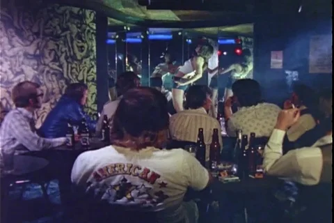 View of men gathered at a strip bar as young woman dances - 1974 Vídeos de archivo 107698288