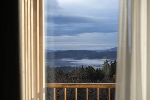 A view of misty mountains through an open window with wooden railings, creating Stock Photos