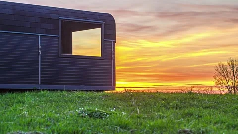 View of a modern cabin in a grassy field at sunset, Latvia. Video stock 340639040