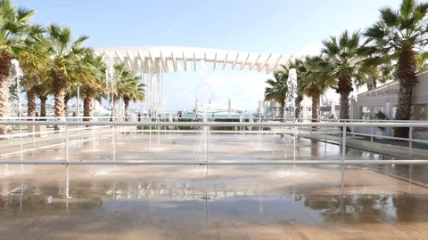 View of a modern fountain, square with multiple sprays, palm trees bordering Stock Footage 106342328