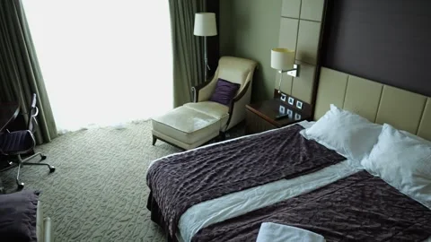 View of modern hotel room interior with neatly arranged bed, soft day lighting a Stock Footage 341974708
