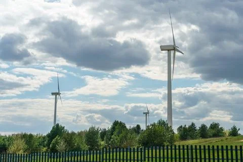 View of a modern windmill against a blue sky. The white blades of the wind tu Stock Photos