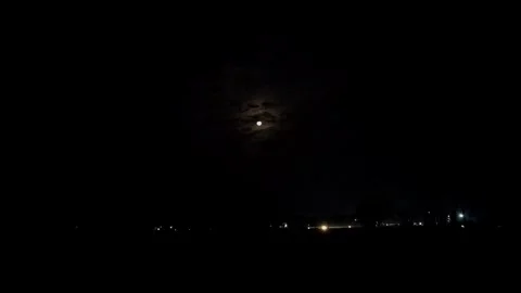View of moon behind thin clouds over moving vehicles on road at night scene Stock Footage 334795527