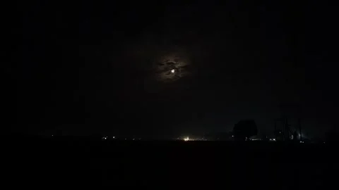 View of moon behind thin clouds over moving vehicles on road at night scene 스톡 동영상 334795543