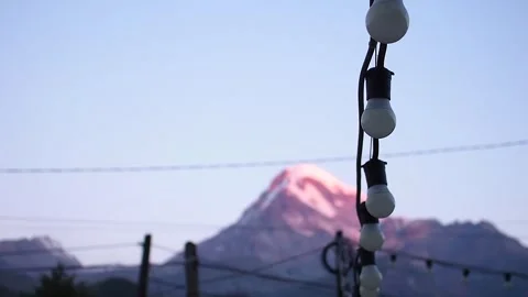 View of Mount Kazbegi in the dawn beams and the night lantern garland Stock Footage 248529760