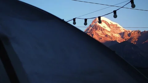 View of Mount Kazbegi in the dawn beams and the gazebo with lantern garland Stock Footage 248530149