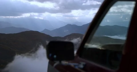 View of the mountain peaks in cloudy weather, next to a vintage SUV. The rays of Stock Footage 239340301