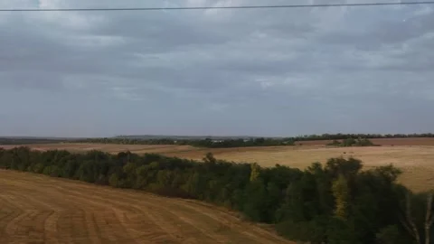 View from a moving train of harvested fields and a line of green trees. The sky Stock Footage 320605930