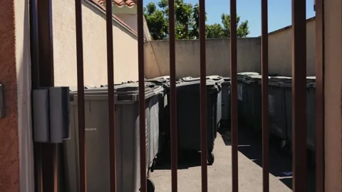 View of multiple garbage containers behind metal bars in an urban area. Stock Footage 336724152