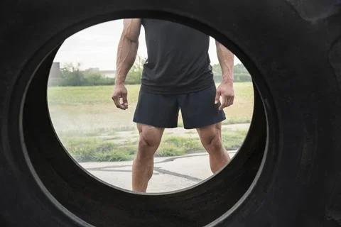 View of muscular Hispanic man wearing tank top through tractor tire he flippe Fotos de archivo