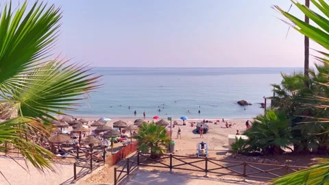View of the Nerja beach with sunbeds and sunshades and people taking a swim Stock Footage 238076078