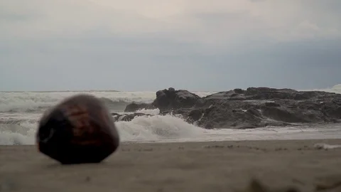 View of the ocean and waves breaking on stones and rocks on sand lies a coconut Stock Footage 126974257