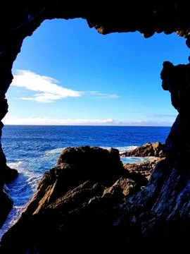 View of ocean through rock opening at coastal location during sunny weather Stock Photos