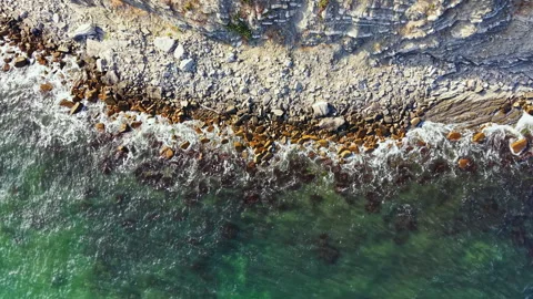 View of ocean waves crashing against rocky shoreline in a coastal area during Stock Footage 341111112