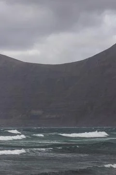 View of Ocean waves rolling on the beach along the shoreline with mountains i Stock Photos