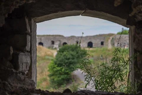 View of an old fort through a stone window framed by greenery in a rural area Stock Photos
