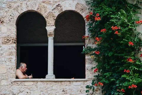 View of an old man sitting in the building an dgreen tree on a wall. Fotos de archivo