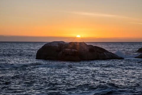 View of orange sunset over ocean with big rock Stock Photos