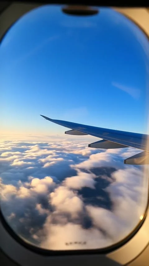 A View out of an airplane window onto a blue sky and clouds and sunlight moving Stock Footage 312895024
