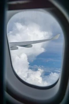 View out of airplane window with clouds at sunset and airplane wing. Stock Photos