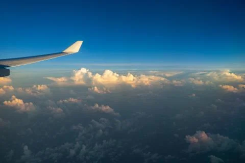 View out of airplane window with clouds at sunset and airplane wing. Stock Photos