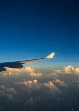 View out of airplane window with clouds at sunset and airplane wing. Stock Photos