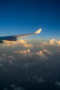 View out of airplane window with clouds at sunset and airplane wing. Stock Photos