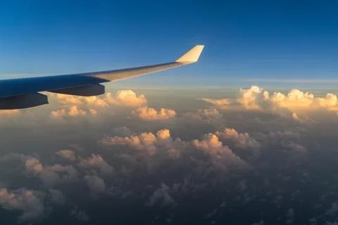 View out of airplane window with clouds at sunset and airplane wing. Stock Photos