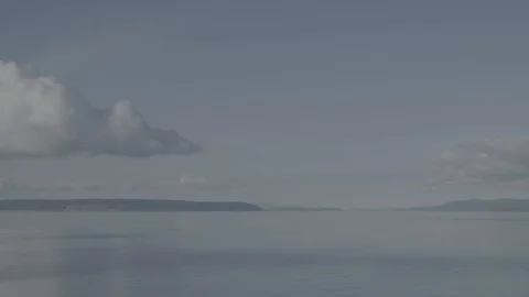 View out over flat sea with clouds and forest islands in distance Stock Footage 127044665