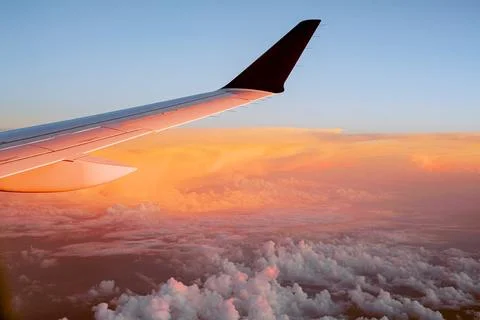 View outside the plane window to the wing and clouds at sunset Stock Photos