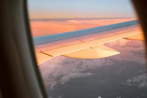View outside the plane window to the wing and clouds at sunset Stock Photos