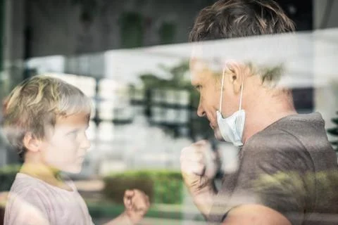 View from outside through window. Father wear white protective mask and little Stock Photos