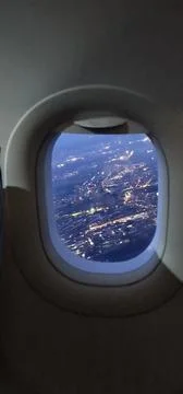 View from an oval airplane window during dusk, glittering city lights scatter Stock Photos