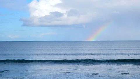 View over breaking waves of pretty rainbow on horizon below white cloud Stock Footage 340332126