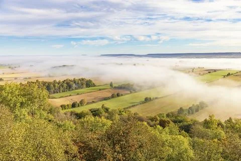 View over a country landscape with a patchwork of fields and mist and with trees 스톡 사진