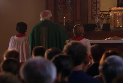 In a view over the heads of a seated congregation, a priest flanked by altar Stock Footage 86832035