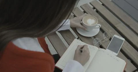 View over the shoulder of the brunette taking notes in her journal while Stock Photos