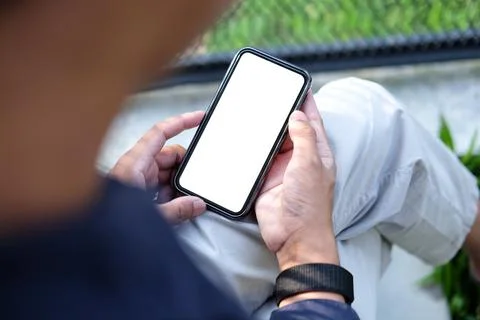 View over shoulder man using smart phone while sitting in the garden. Stock Photos