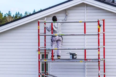 View of painter working on scaffolding while painting exterior wall Stock Photos