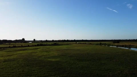 View of a Paraglider Flying at Sunset Over a River and Scenic Green Fields Drone Stock Footage 297624571