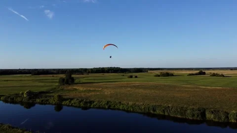 View of a Paraglider Flying at Sunset Over a River and Scenic Green Fields Drone Vídeos de archivo 297624574