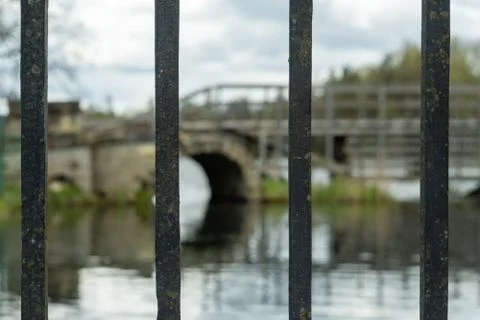 View of the park through the iron bars. The lake, the bridge. Daytime. Stock Photos