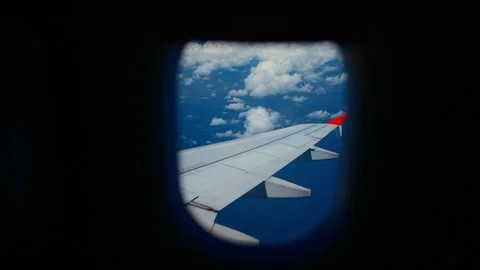 View from passenger seat through airplane porthole, plane wing and white clouds. Stock Footage 346531474