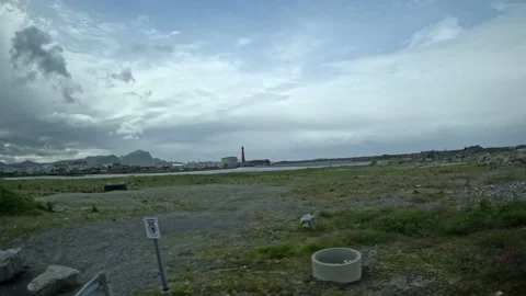 View past coastal field, red lighthouse, and town skyline in Andenes Norway Vidéo 342755592